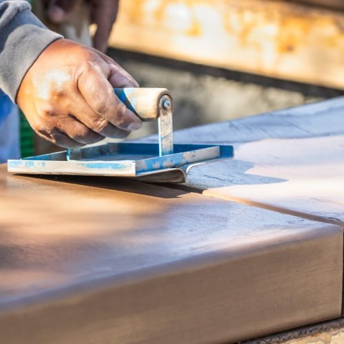 Construction Worker Using Hand Groover On Wet Cement Forming Coping Around New Pool.