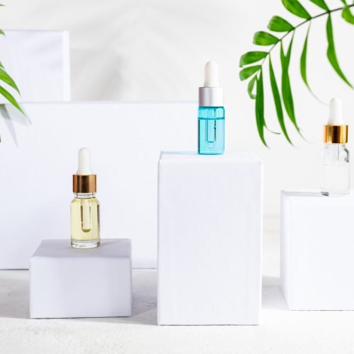 Natural cosmetics products in bottles with dropper, skin care beauty products - serum, lotion, herbal cosmetic on white podium with green leaf. Serum for woman facial skin on white stand. Copy space